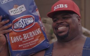 Photograph of Vince Wilfork. He is smiling and holding a bag of Kingsford charcoal briquets.