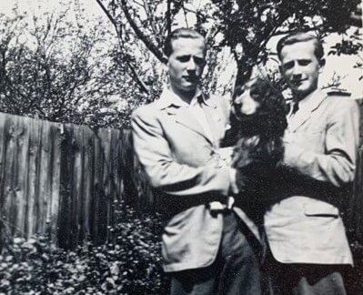 Schwarz-Weiß-Foto aus den 1950er Jahren von 2 elegant gekleideten jungen Männern. Sie stehen vor einem Zaun, halten einen Hund und haben einen Baum im Rücken. Die Männer sind der Vater von George Coleman und sein Zwillingsbruder.