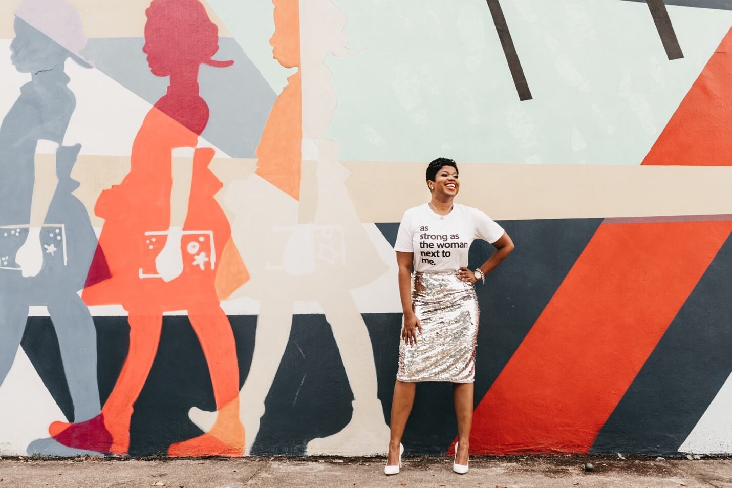 Powerful smiling Black woman stood in front of mural of Ruby Bridges.