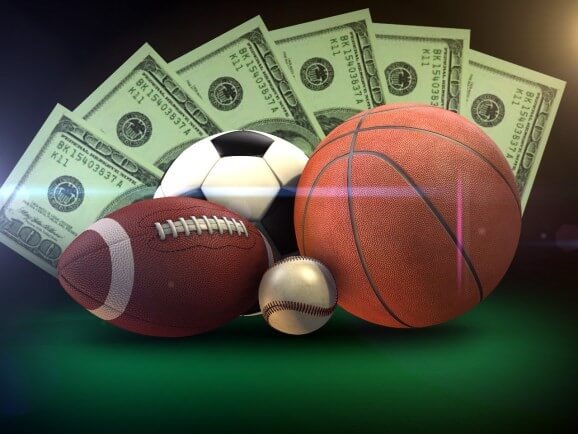 Fou different sports balls in front of a fan of dollar bills.