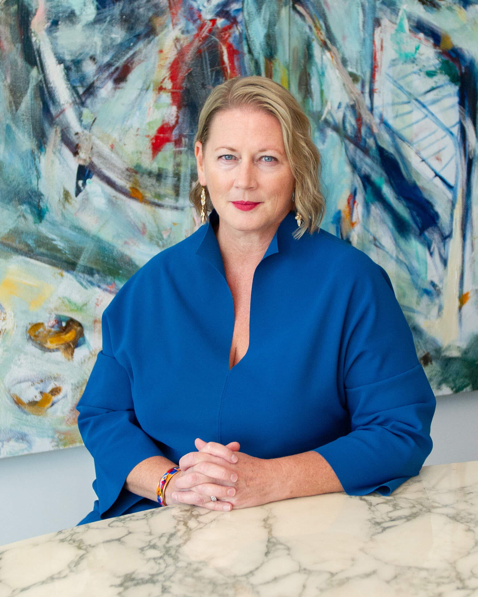 Plan de tête du PDG Virginia Devlin. Elle a des cheveux blonds aux épaules, des yeux bleus et porte un haut bleu. Elle est assise devant un mur aux motifs vifs.