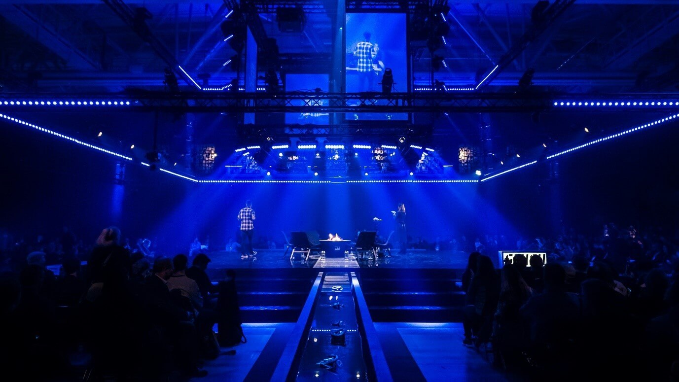 Stage at CES with blue background with a man stood presenting with his back to the crowd.